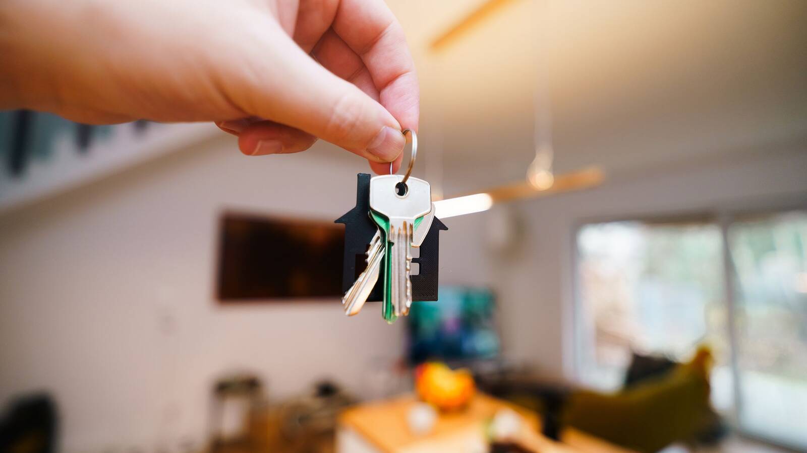 A hand holding a set of house keys inside a bright, modern living room