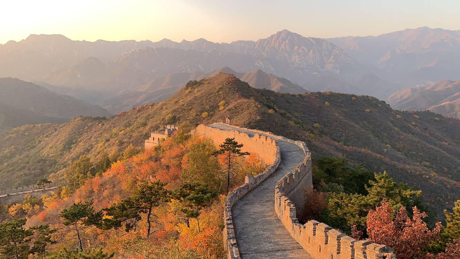 The Great Wall of China winding over hills with autumn trees near Beijing, with mountains behind in evening light